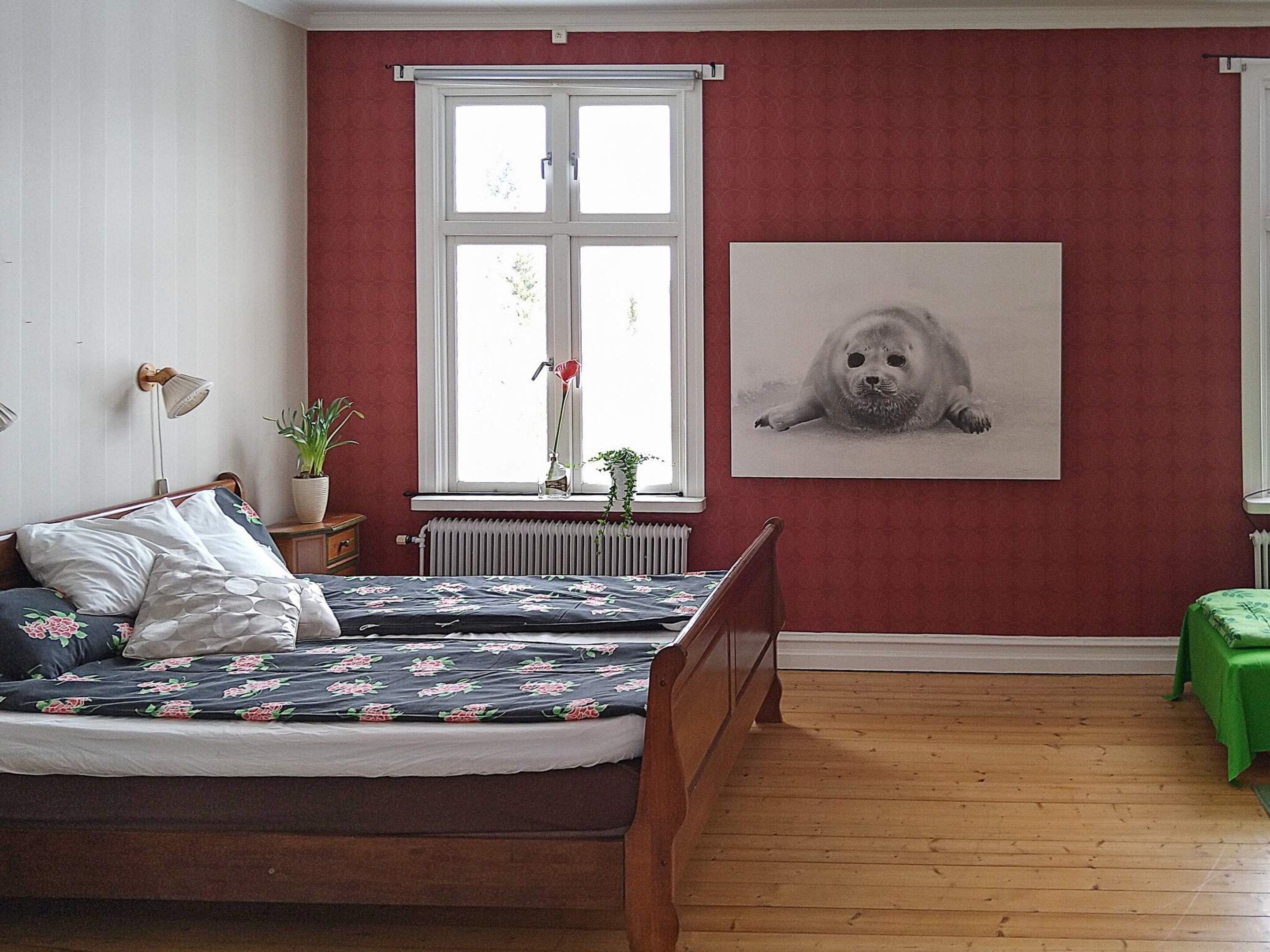 A bedroom with a bed, a radiator, a window, and a framed picture on the wall.