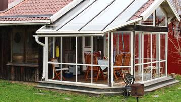 A conservatory with a glass roof, wooden chairs, and a grill outside.