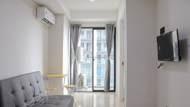 A modern living room with a grey sofa, a small table, and a TV mounted on the wall. - Comfort 2Br At Daan Mogot City Apartment (Jakarta)