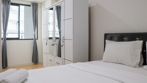 A bedroom with a bed, a wardrobe, and a window with curtains. - Comfort 2Br At Daan Mogot City Apartment (Jakarta)