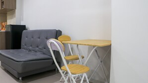A small room with a grey sofa, a wooden table, and a white chair. - Comfort 2Br At Daan Mogot City Apartment (Jakarta)