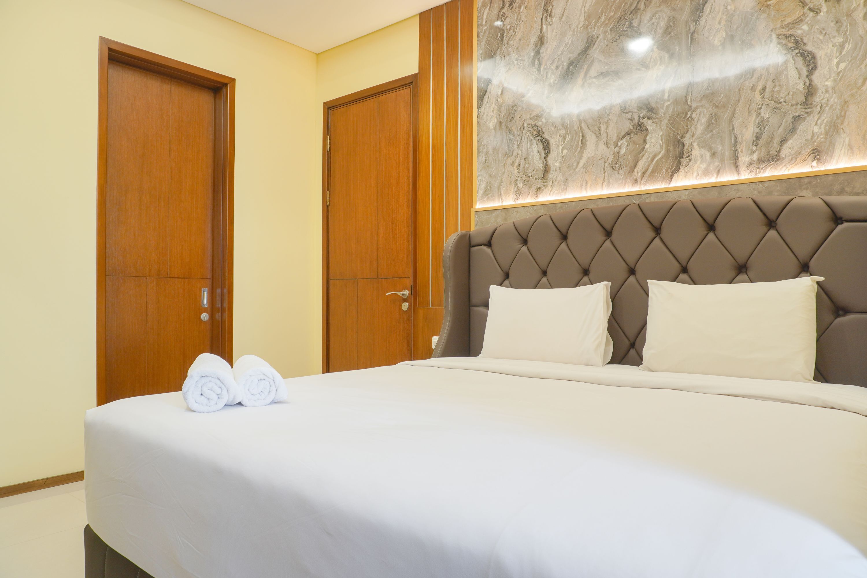 Habitación de hotel con una cama grande, dos puertas de madera y una pared de mármol.