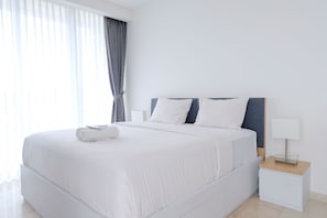 A modern hotel room with a large bed, white bedding, a nightstand with a lamp, and a view of the outside through sheer curtains.