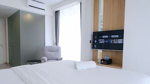 A modern hotel room with a large bed, a grey armchair, a TV mounted on the wall, and a minibar. - Best Deal Studio Room With Private Jaccuzi At Art Deco Apartment (Bandung)
