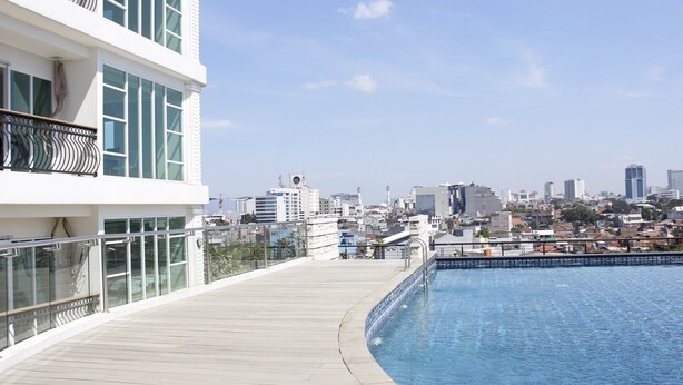 Piscina en la azotea con vistas a la ciudad, barandilla de cristal y un edificio moderno con balcones.