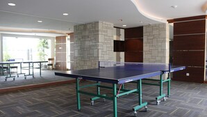 Una mesa de ping pong en una habitación con alfombra estampada, pared de piedra y una puerta con panel de madera.