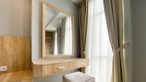 A modern bathroom with a wooden vanity, a mirror, and a beige ottoman. - Simply Look And Comfort 1Br Vasanta Innopark Apartment (Cikarang)