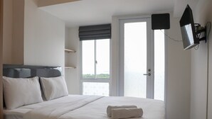 A hotel room with a bed, a window, a door, and a mounted TV. - Best Choice And Cozy Studio Apartment At Tokyo Riverside Pik 2 (Teluknaga)