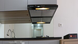 A modern kitchen with a black range hood, a white refrigerator, and a wooden cabinet. - Comfort Stay Studio Apartment At Tokyo Riverside Pik 2 (Teluknaga)