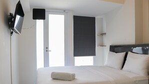 A hotel room with a bed, a TV mounted on the wall, a door, and a window with a blind. - Comfort Stay Studio Apartment At Tokyo Riverside Pik 2 (Teluknaga)