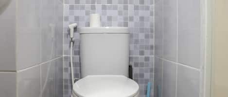 Et badeværelse med toilet, toiletpapirholder og hårtørrer.