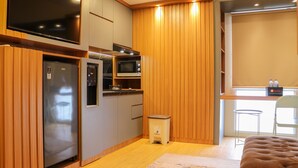 A compact kitchen with built-in appliances, a small stool, and a window with blinds. - Well Furnished And Cozy 2Br Tokyo Riverside Pik 2 Apartment (Teluknaga)
