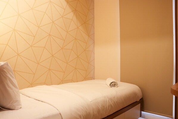 A single bed with a geometric patterned wall behind it.