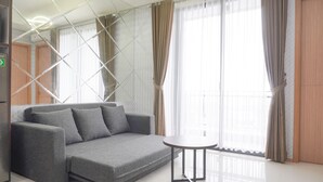 A modern living room with a grey sofa, a small round table, and large windows with curtains.