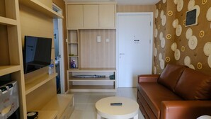 Ein Wohnzimmer mit einem braunen Ledersofa, einem kleinen runden Tisch, einem Fernseher auf einem Holzständer und einer Wand mit Muster.