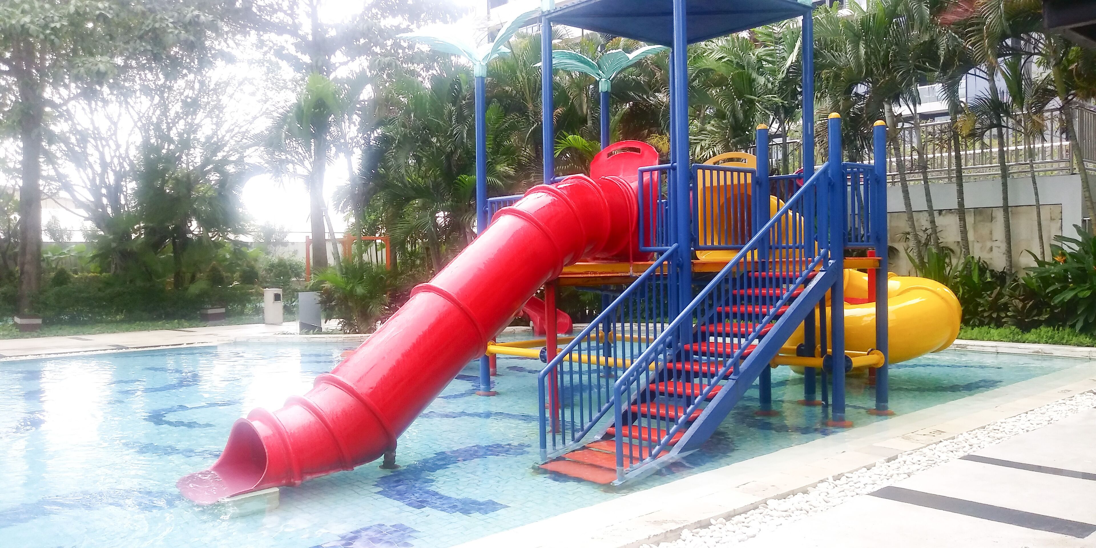 Zona de juegos infantiles con un tobogán rojo y estructuras de juego en amarillo y azul.