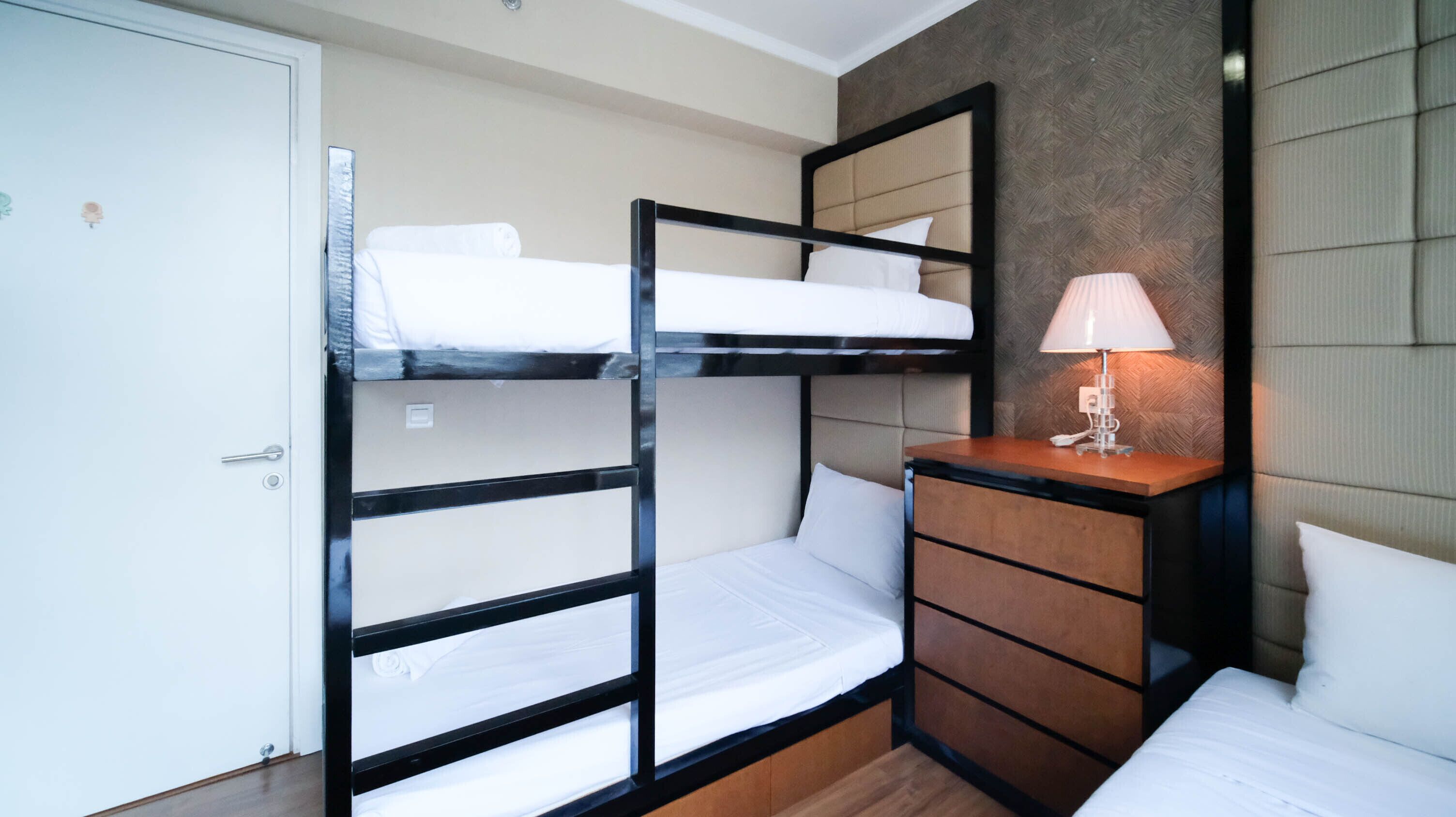 A bunk bed room with a wooden dresser and a lamp.
