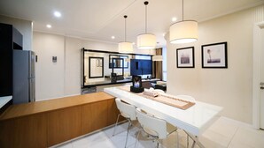 A modern hotel kitchen with a central island, white bar stools, pendant lighting, and framed artwork on the walls. - Spacious 2Br At The Via And The Vue Apartment Surabaya (Surabaya)