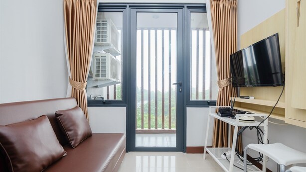 A room with a brown leather sofa, a TV mounted on the wall, a small table with electronic devices, and a sliding glass door leading to a balcony.