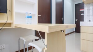 A small, light-colored wooden table with a metal support, a white stool, and a water bottle on a shelf.