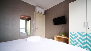Ein Hotelzimmer mit Bett, Kleiderschrank, Fernseher und einem kleinen Tisch mit Pflanze.