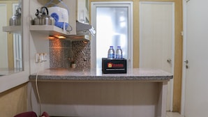 A kitchen with a countertop, a kettle, a water dispenser, and a box labeled 'Travelio'. - Fancy And Nice 2Br Apartment At Green Pramuka City (Jakarta)