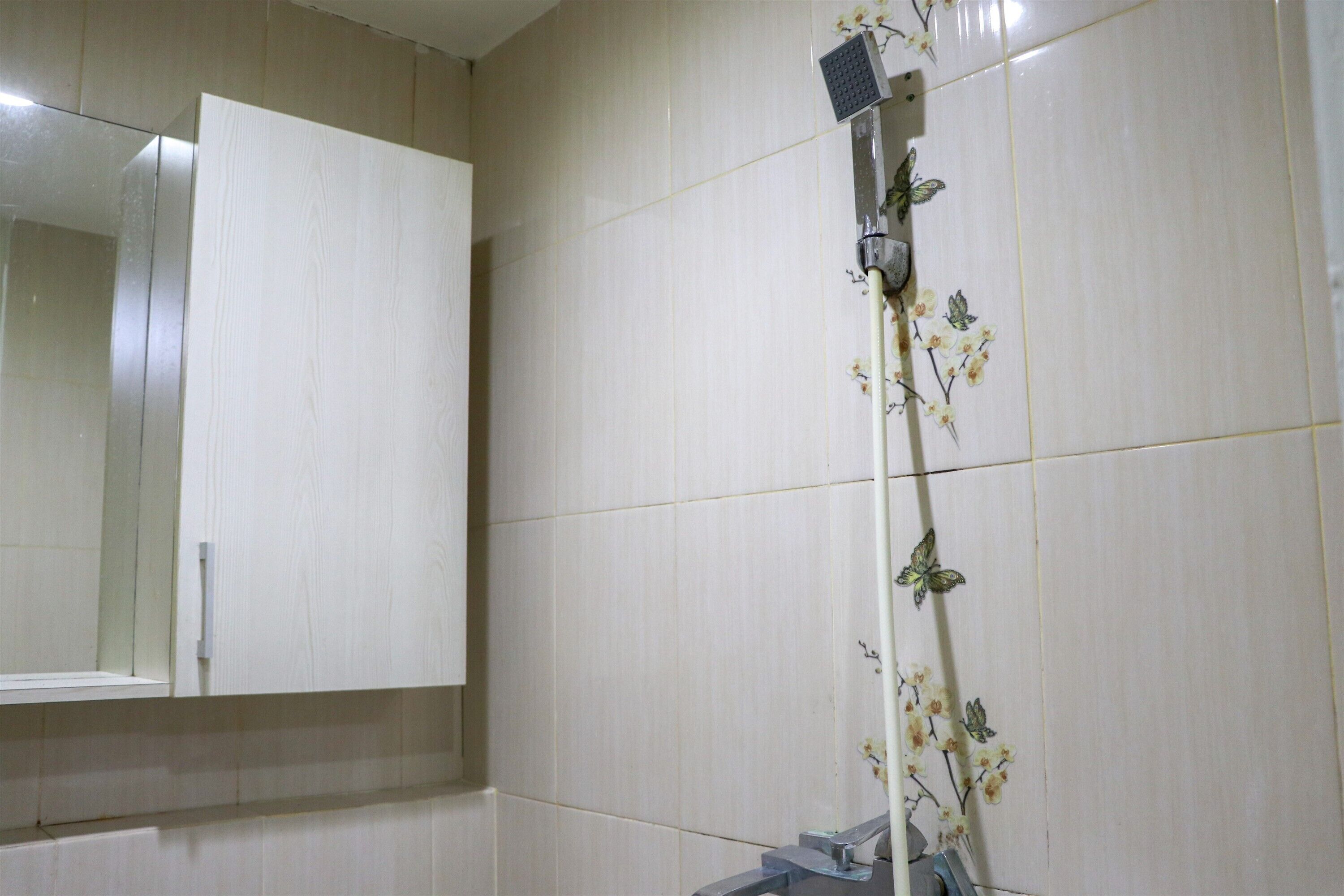 Een badkamer met witte tegels, een douche met bloemendecoratie en een spiegel boven een kastje.