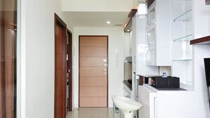A modern kitchen with white cabinets, a stainless steel sink, and a wooden door in the background. - Comfort 1Br At Vida View Makassar Apartment (Makassar)