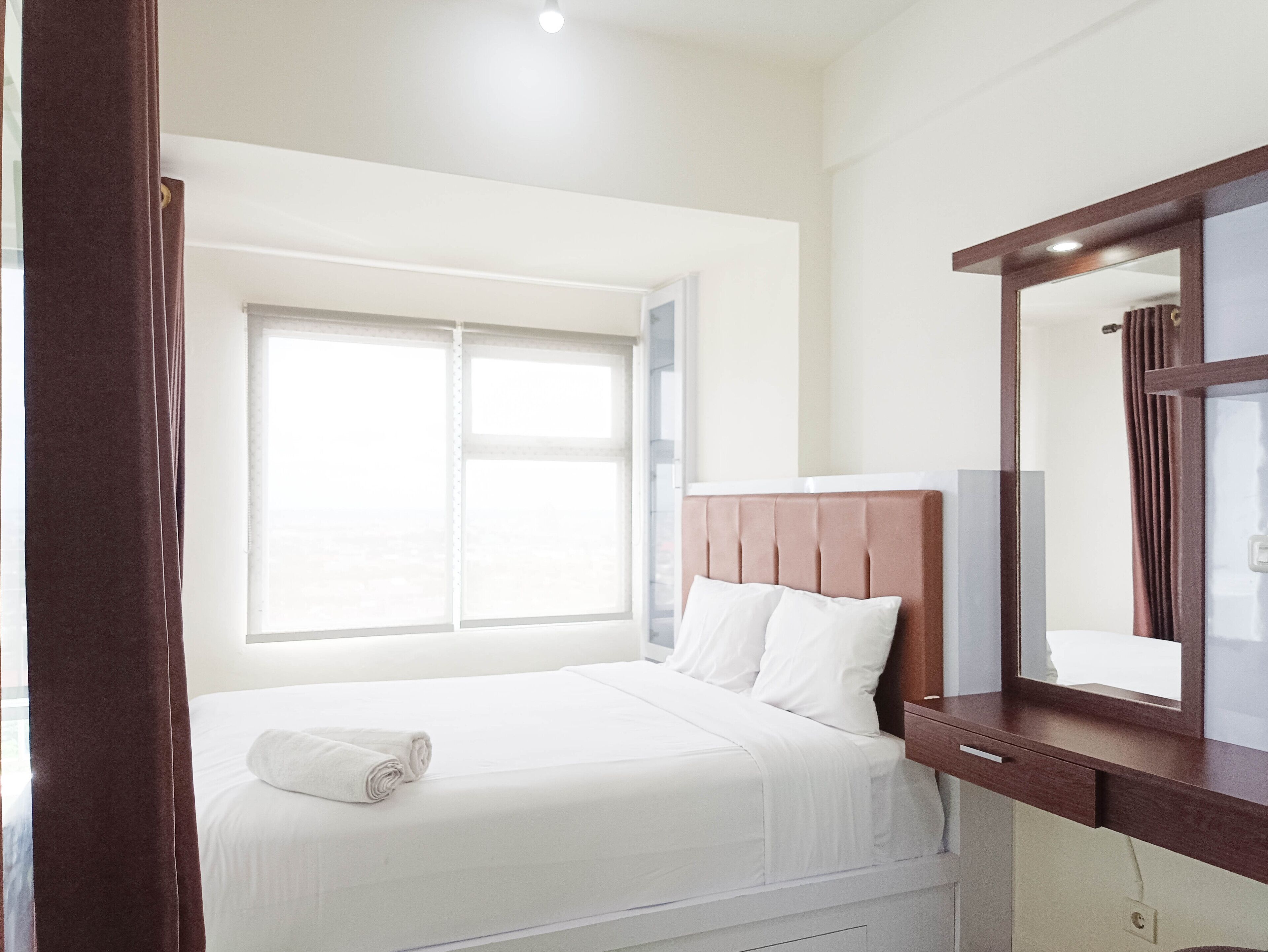 A hotel room with a bed, a large window, a wooden dresser, and a mirror.