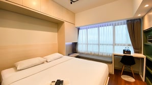 Une chambre d’hôtel avec un grand lit, un bureau avec une chaise, une fenêtre avec des rideaux et une petite table sur laquelle sont posées deux bouteilles.