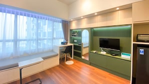 Une chambre d’hôtel moderne avec un plancher en bois, un bureau avec une chaise, une télévision, un mini-réfrigérateur et un mur d’accent vert.