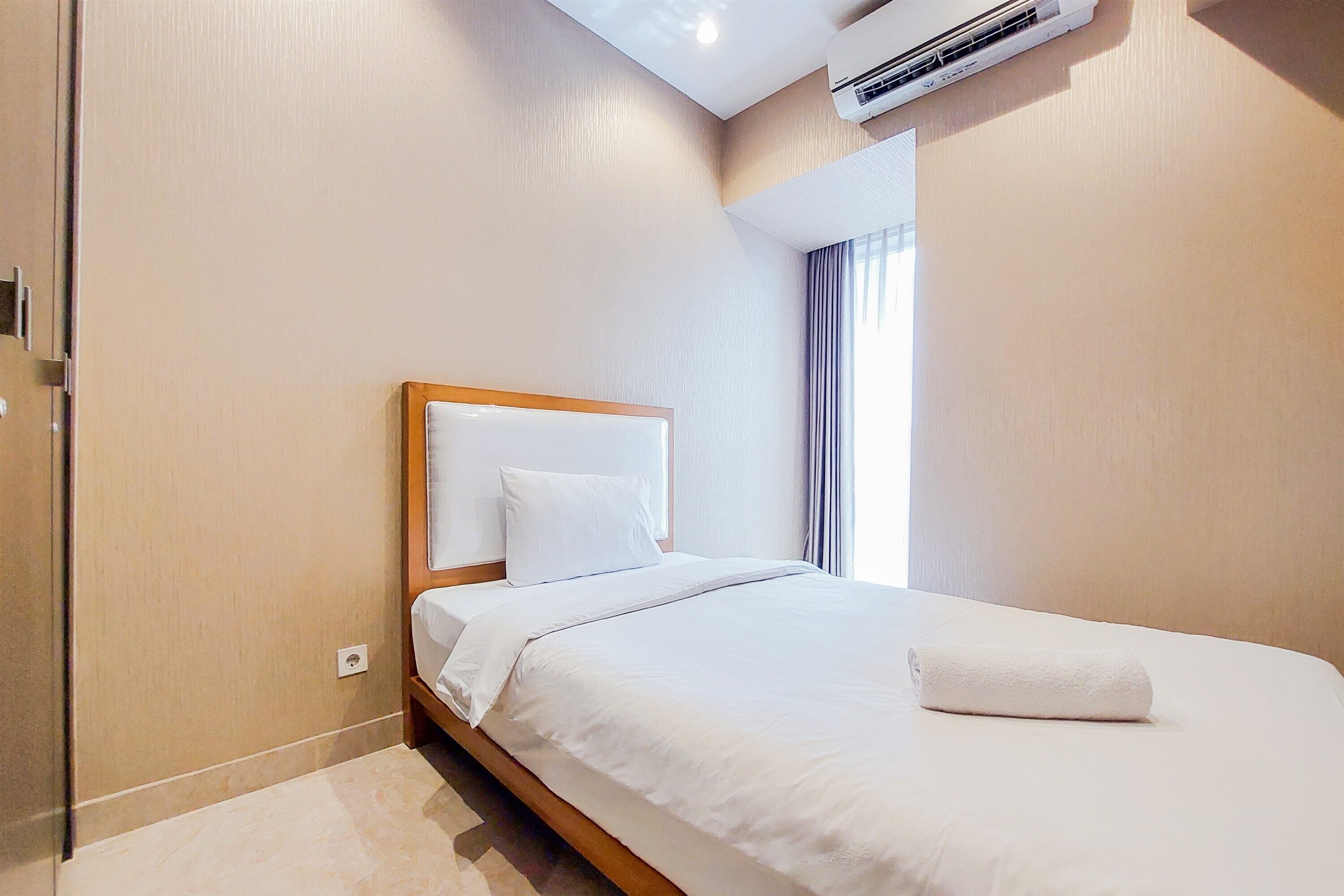 Een keurig opgemaakt bed met witte lakens in een hotelkamer met beige wanden en een houten hoofdbord.