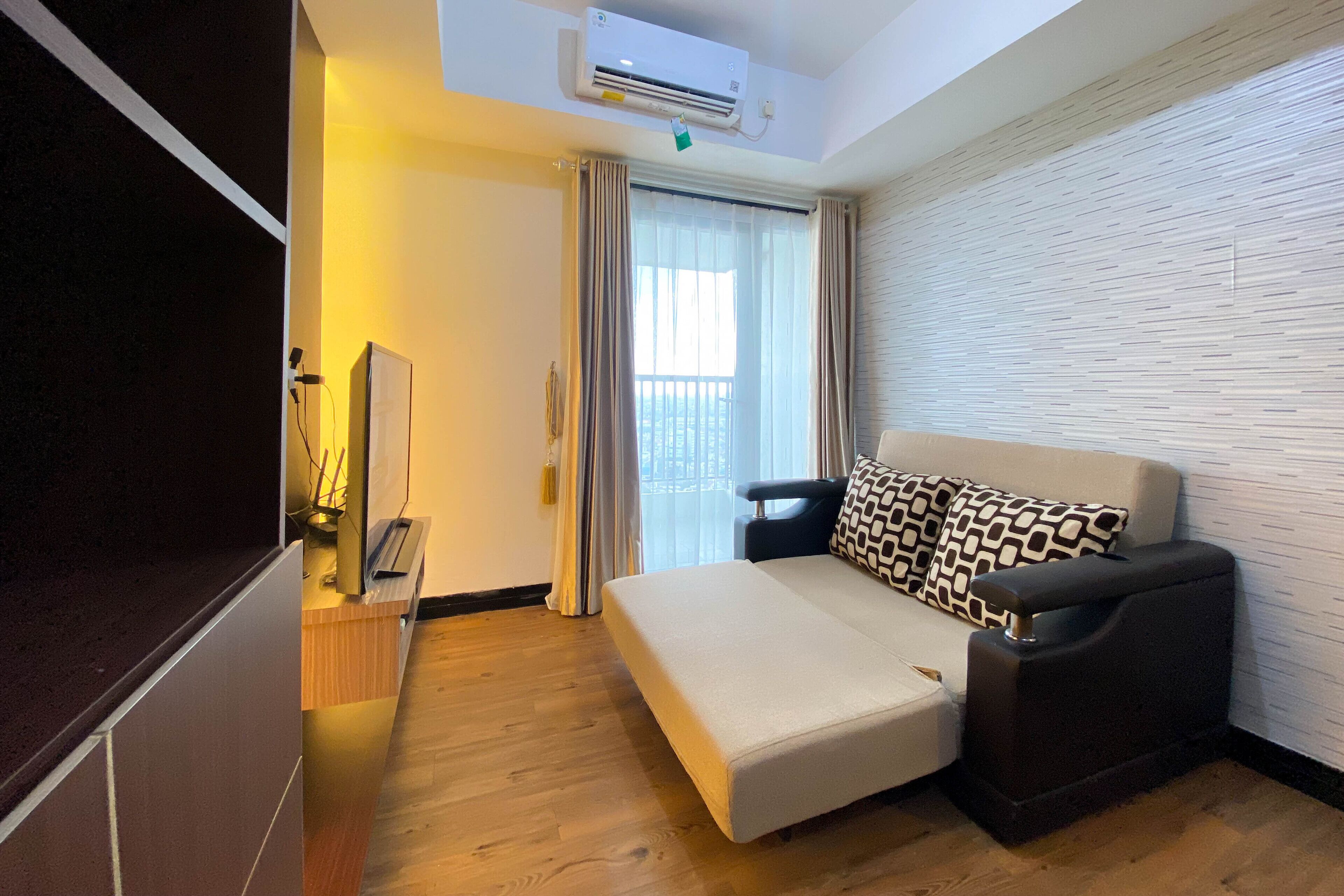 Una habitación de hotel moderna con sofá cama, televisor de pantalla plana, escritorio con lámpara y ventana con cortinas.