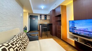 Una sala de estar moderna con un sofá, un televisor y una cocina al fondo.