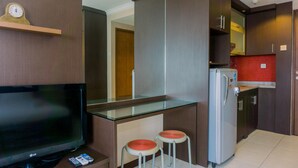 Eine moderne Küche mit Fernseher, zwei Barhocker, einem Kühlschrank und einer Uhr auf einem Regal.
