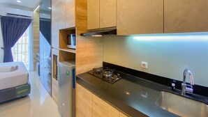 A modern kitchen with a black countertop, stainless steel sink, and wooden cabinets. - Elegant And Homey Studio Ciputra World 2 Apartment (Jakarta)