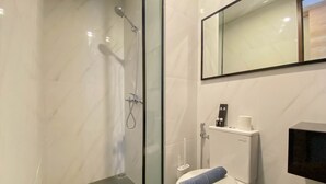 A modern bathroom with a glass-enclosed shower, a toilet with a blue towel, and a black soap dispenser on the wall. - Elegant And Homey Studio Ciputra World 2 Apartment (Jakarta)