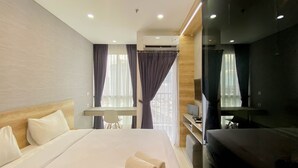 A hotel room with a large bed, a desk, a chair, a TV, and an air conditioning unit. - Elegant And Homey Studio Ciputra World 2 Apartment (Jakarta)