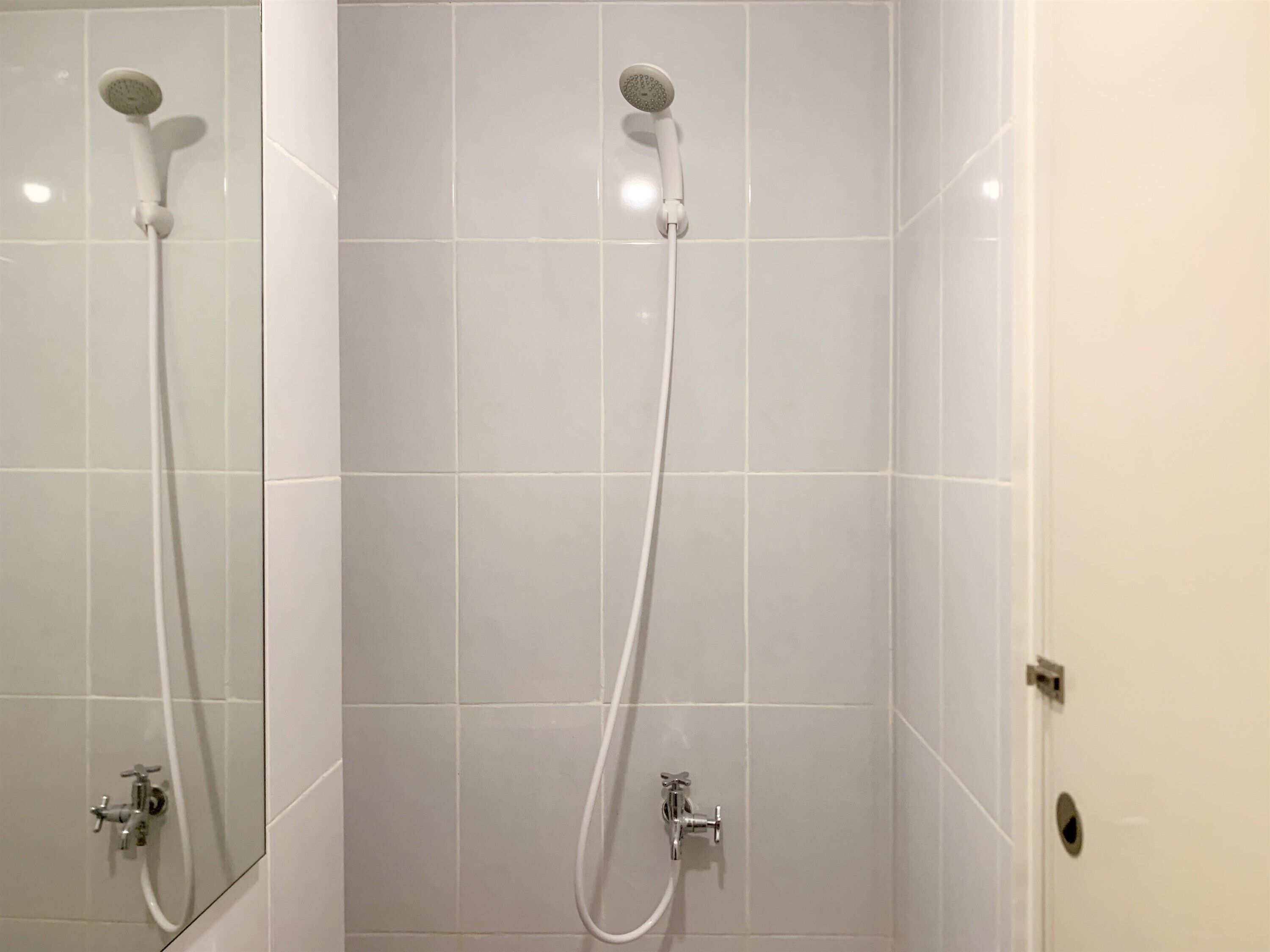 A bathroom with two showerheads and faucets on white tiled walls.