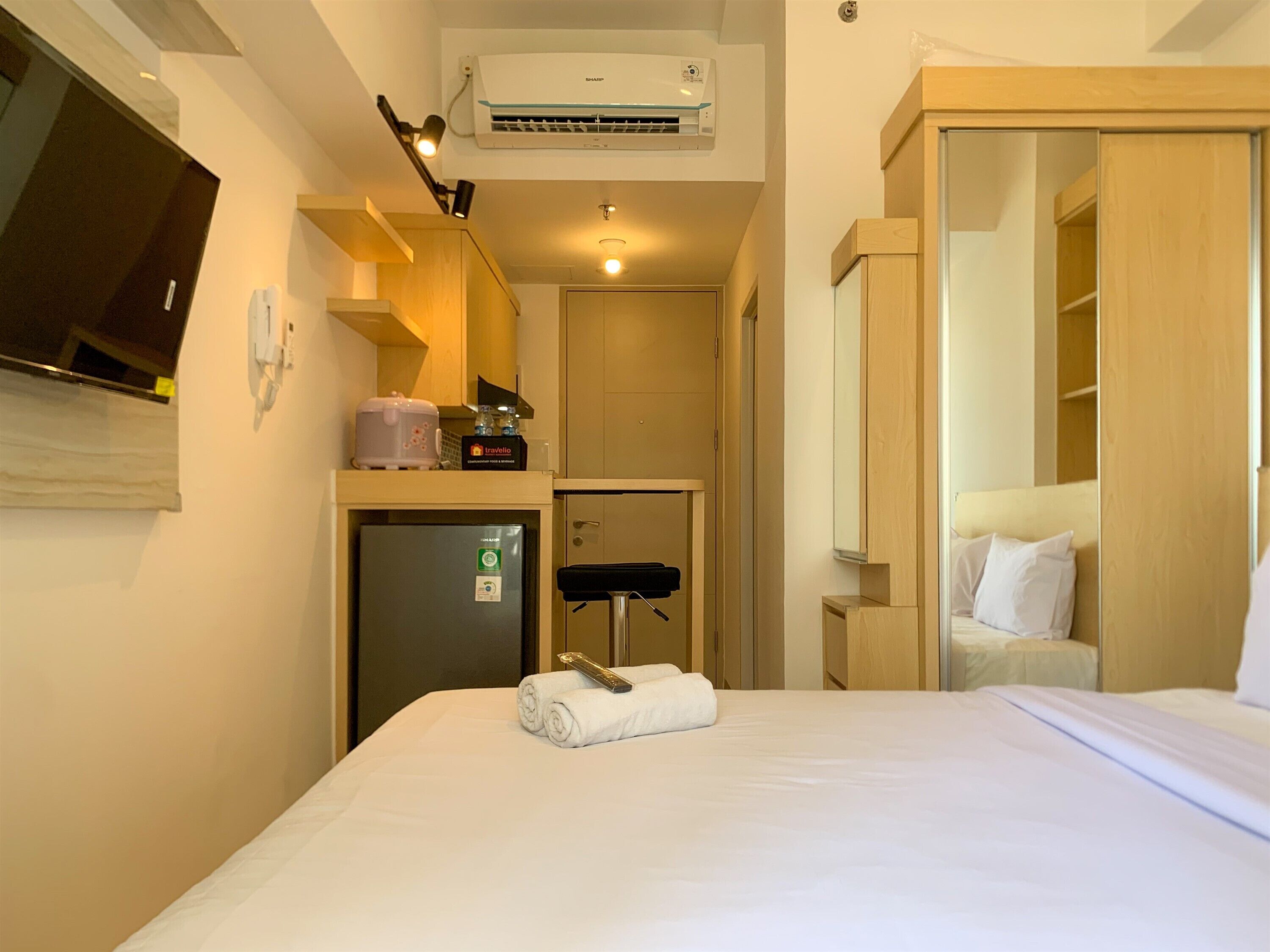 A hotel room with a bed, a desk with a computer, a small fridge, a microwave, a TV, and a wardrobe.