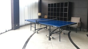 A ping pong table in a modern room with a large window, a lamp, and a seating area. - Homey 2Br At Braga City Walk Apartment (Bandung)