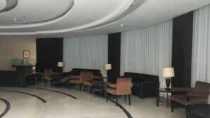 A lobby with a modern design, featuring a reception desk, several sofas, and chairs arranged for guests. - Homey 2Br At Braga City Walk Apartment (Bandung)