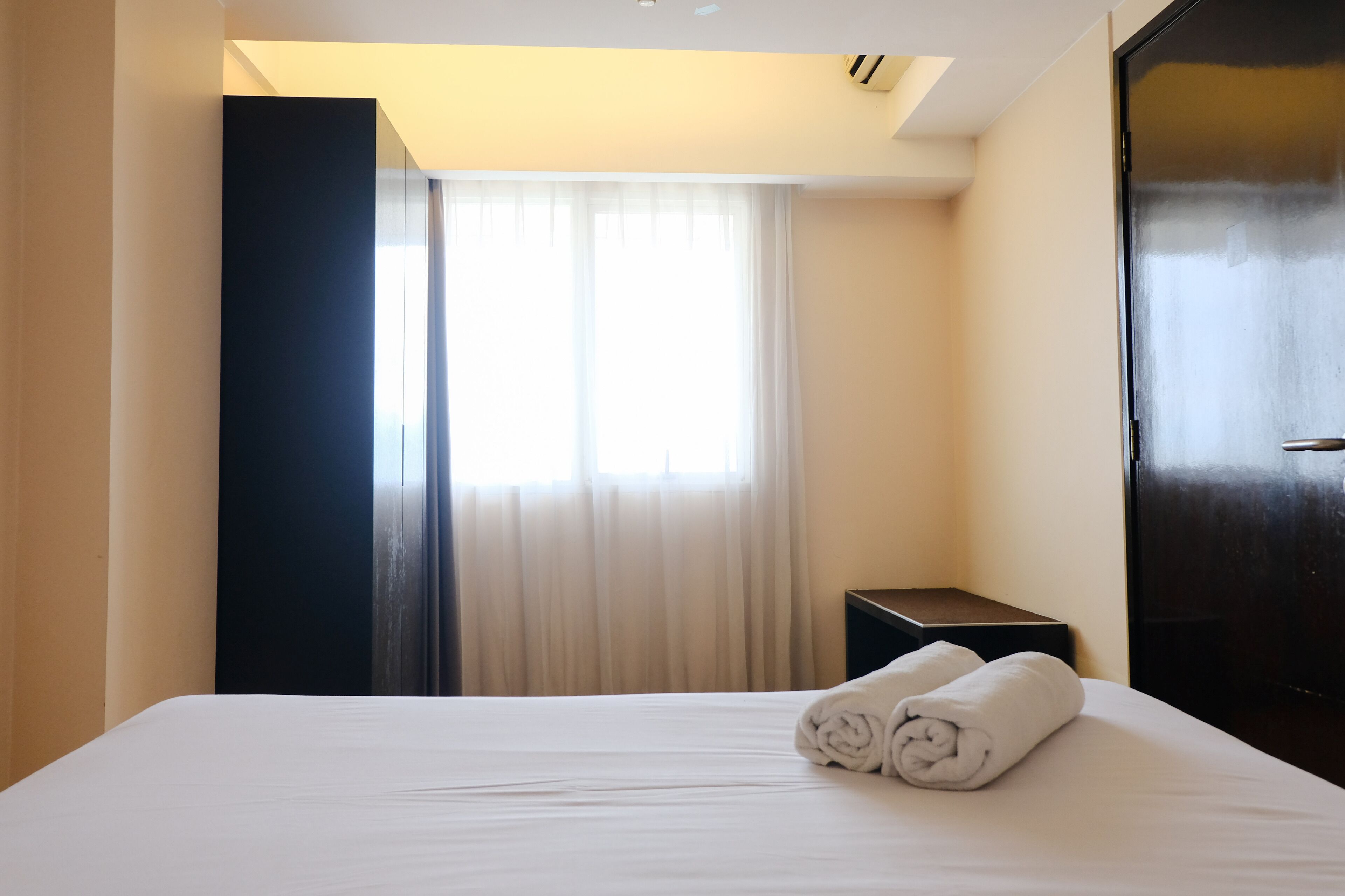 Une chambre d’hôtel avec un lit, une table de chevet, une porte sombre et une fenêtre avec des rideaux.