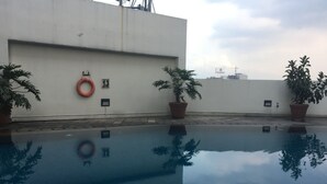 An outdoor swimming pool with potted plants and a lifebuoy on a white wall. - Homey 2Br At Braga City Walk Apartment (Bandung)