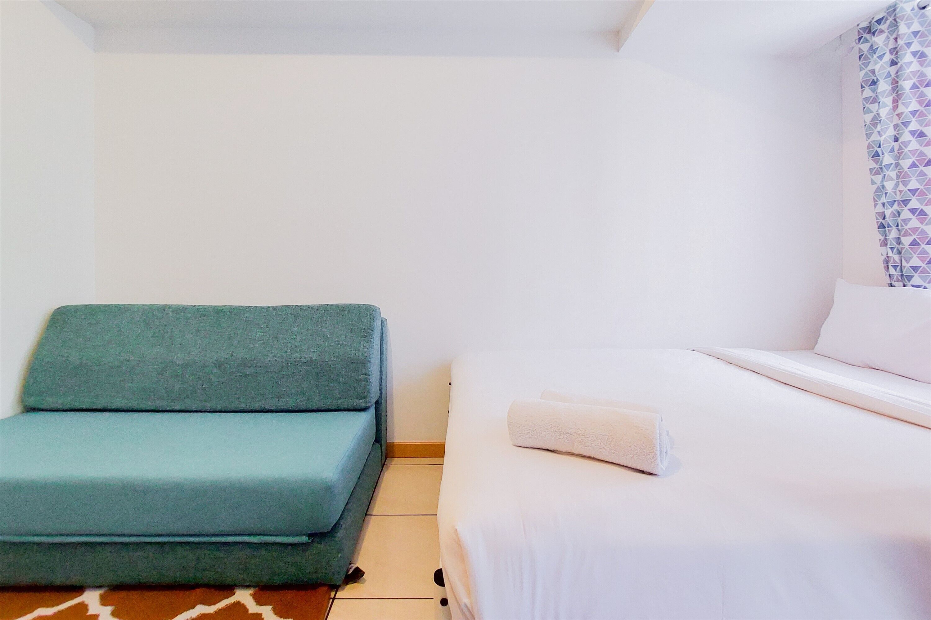 A small, clean room with a bed, a green sofa, and a patterned curtain.