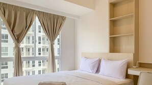 A hotel room with a large bed, a desk, and a view of buildings through the window. - Relaxing And Warm 2Br At Tokyo Riverside Pik 2 Apartment (Teluknaga)