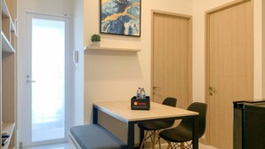 A compact room with a small table, two chairs, a bench, a shelf with a plant, and a door. - Relaxing And Warm 2Br At Tokyo Riverside Pik 2 Apartment (Teluknaga)