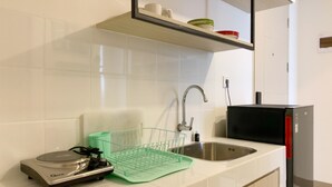 A kitchen with white tiles, a stainless steel sink, a green dish rack, and a black microwave. - Relaxing And Warm 2Br At Tokyo Riverside Pik 2 Apartment (Teluknaga)