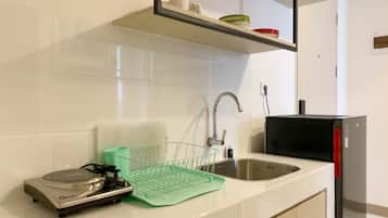 Uma cozinha com azulejos brancos, uma pia de aço inoxidável, um escorredor de louça verde e um micro-ondas preto.
