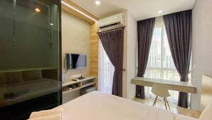 A hotel room with a bed, a TV, a desk, and a balcony with curtains. - Restful And Comfortable Studio At Ciputra World 2 Apartment (Jakarta)